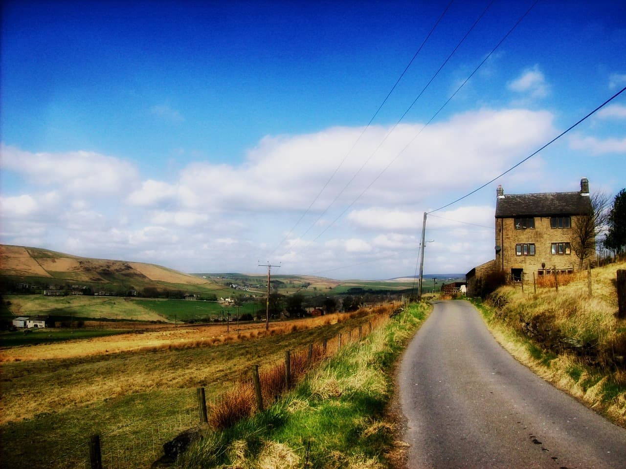 A country road between dry-stone walls and fields, a stone house ahead